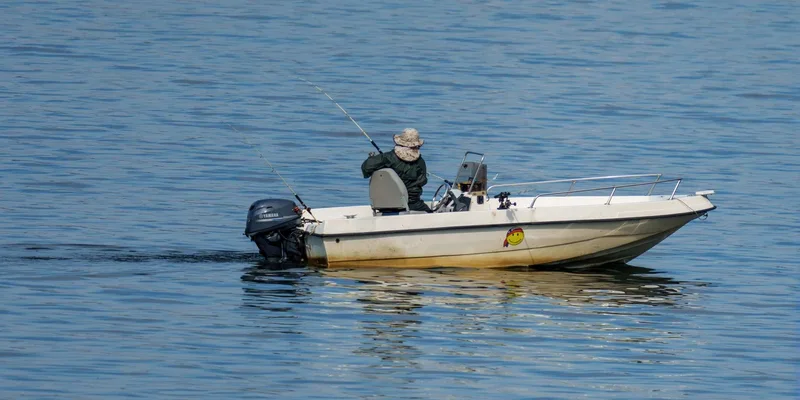 A fisherman enjoying a peaceful day fishing on a motorboat in calm, blue waters