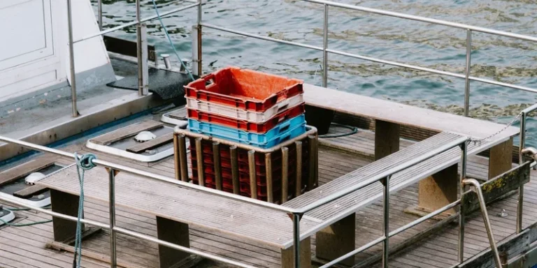 Close-up view of an empty fishing boat's wooden deck with stacked colorful crates and a calm water background