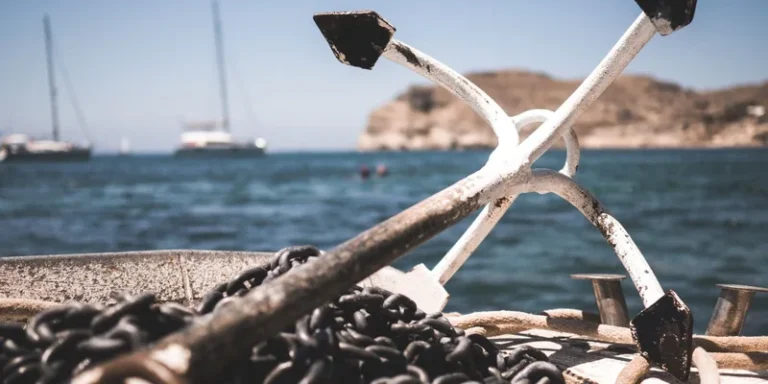 Close-up of boat anchor and chains with ocean and sailboats in the background
