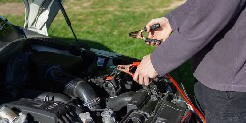 Close-up of mechanic using jumper cables to jump-start a car battery outdoors