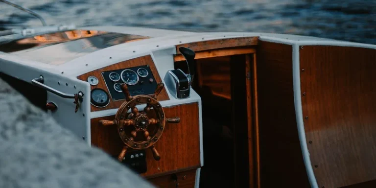 Close-up of a classic wooden helm on a boat steering through calm waters at sunset