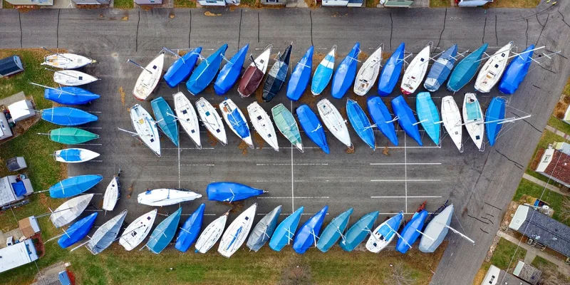 Aerial shot of numerous sailboats covered with blue tarps in an urban marina parking area