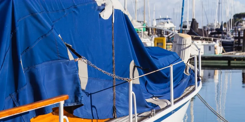 Close-up of a sailboat with blue tarp cover docked in a marina on a sunny day