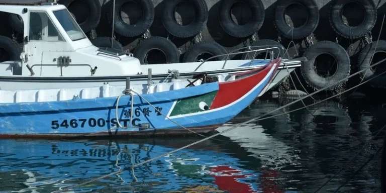 A vibrant fishing boat docked against a wall lined with tire fenders