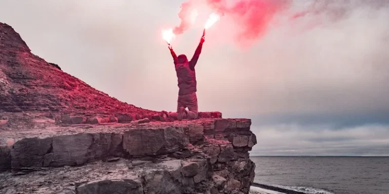 Dramatic scene of a man with flares signaling for help on a rocky cliff by the ocean