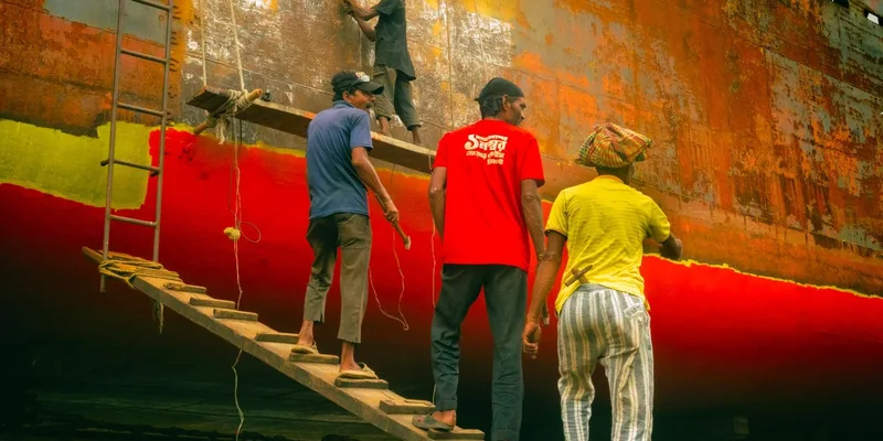 Four workers refurbishing the hull of a rusted ship in a dockyard