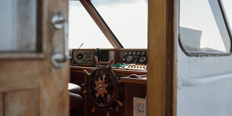 A detailed view of a vintage boat helm featuring a wooden steering wheel and control panels