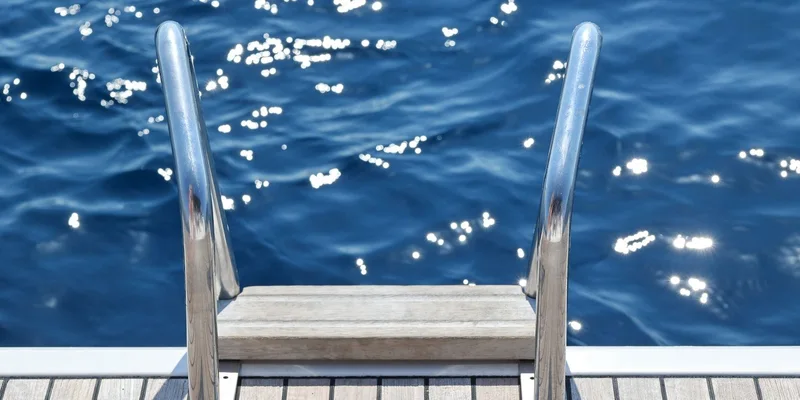 A metal ladder descending from a pier into calm, sunlit water