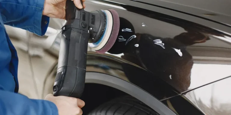 Hands using a polishing machine on a car's surface in a garage setting