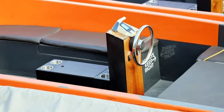 Close-up view of a sleek orange boat interior featuring a wooden steering wheel and seating