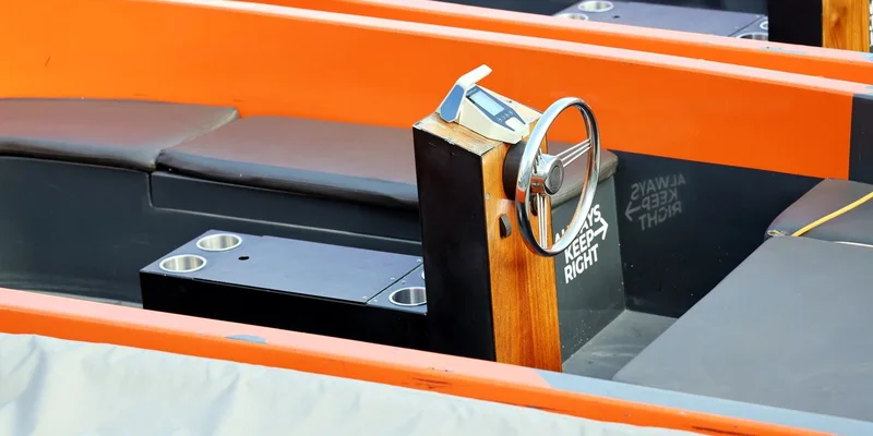 Close-up view of a sleek orange boat interior featuring a wooden steering wheel and seating