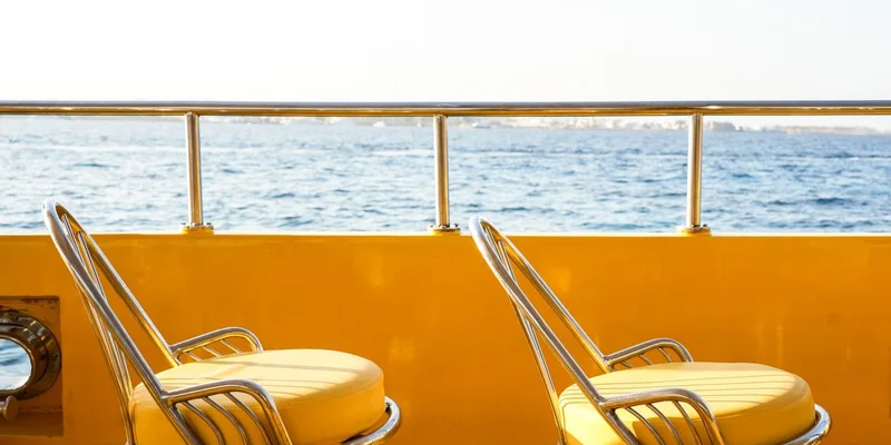 Two bright yellow deck chairs on a boat with a serene ocean view under clear skies