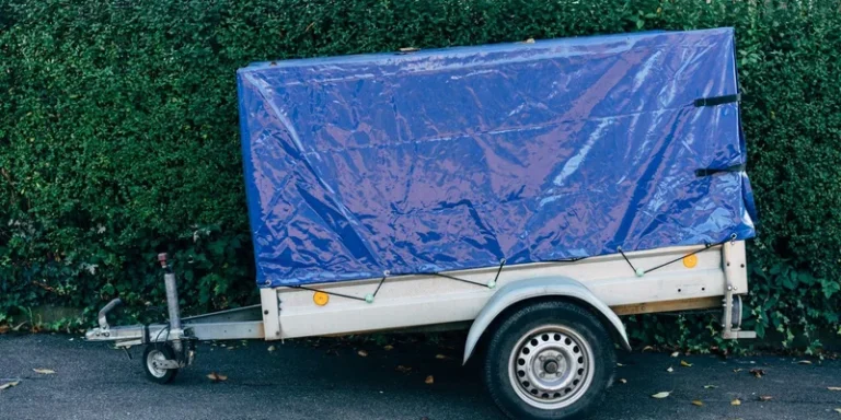 A blue tarpaulin-covered trailer parked on a roadside against a hedge