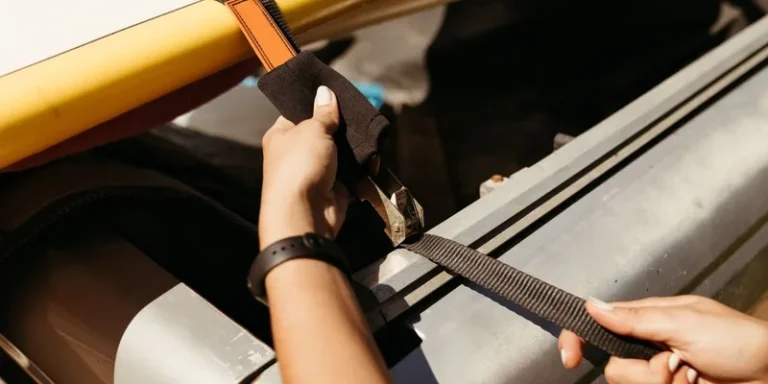 Hands securing a yellow surfboard onto a vehicle roof with straps on a sunny day