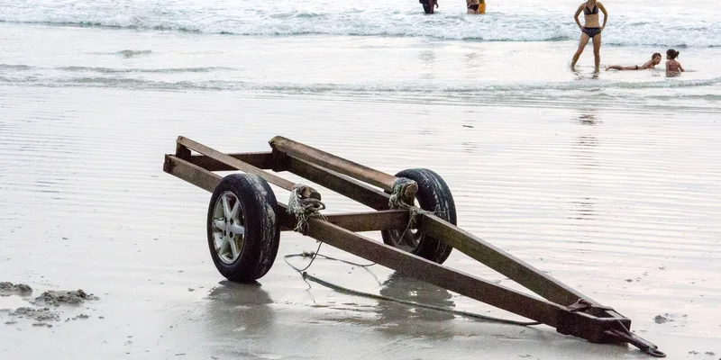 Rusty trailer on Langkawi beach with people enjoying the ocean in Malaysia