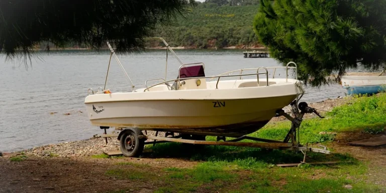 A small boat on a trailer by a tranquil lakeside surrounded by lush greenery