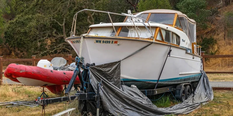 A white yacht on a trailer beside a red inflatable boat, set outdoors