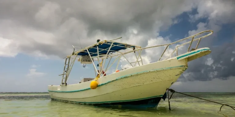 A white boat anchored in shallow waters under an overcast sky