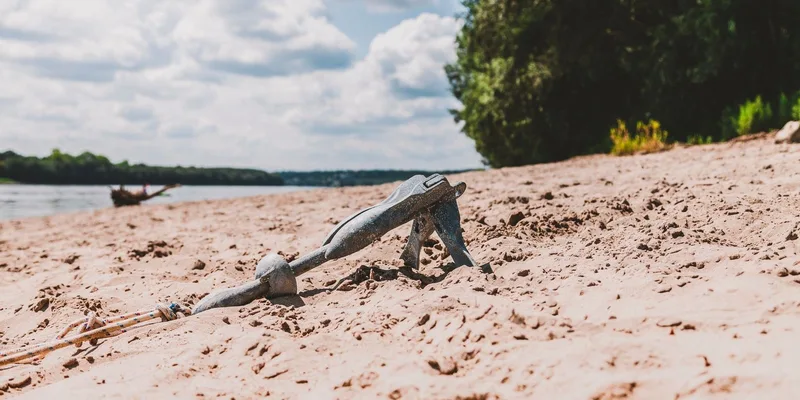 A scenic beach view with a metal anchor on sandy shores under clear blue skies