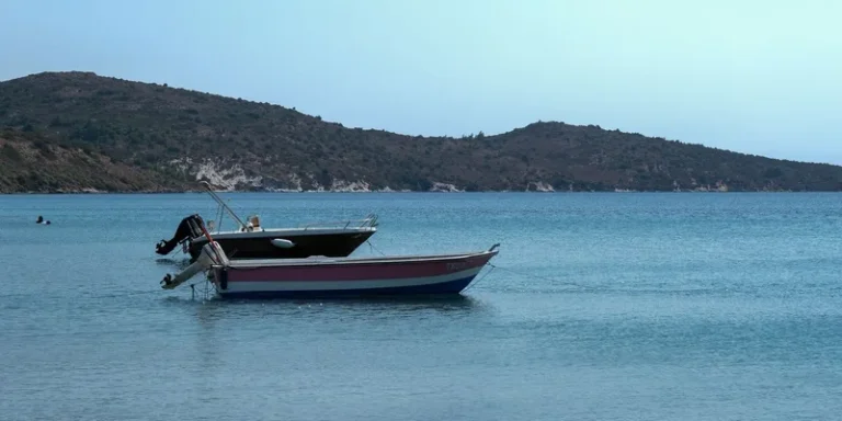 Two boats anchored in a calm, turquoise bay with hilly island backdrop