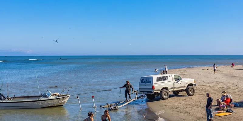 A family enjoys a sunny day at the beach while a truck assists with a boat trailer