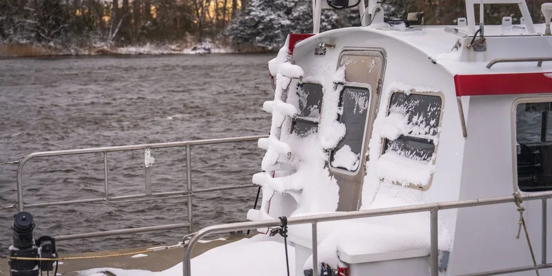 A snowy boat on a river with frosty trees and bridge background