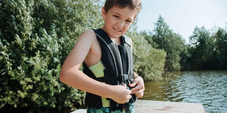 Happy child in a life jacket smiling at the camera while standing on a lakeside jetty