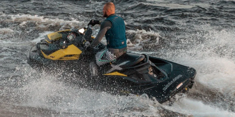 A man wearing a life vest rides a jet ski across choppy waters
