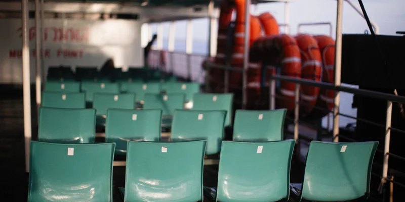 Rows of unoccupied teal seats on a ferry with lifebuoys during a serene day