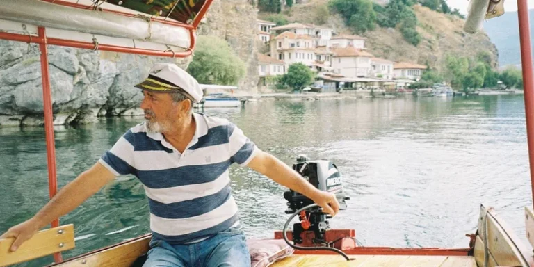 A captain navigates a boat on a tranquil lake, surrounded by picturesque hillside houses