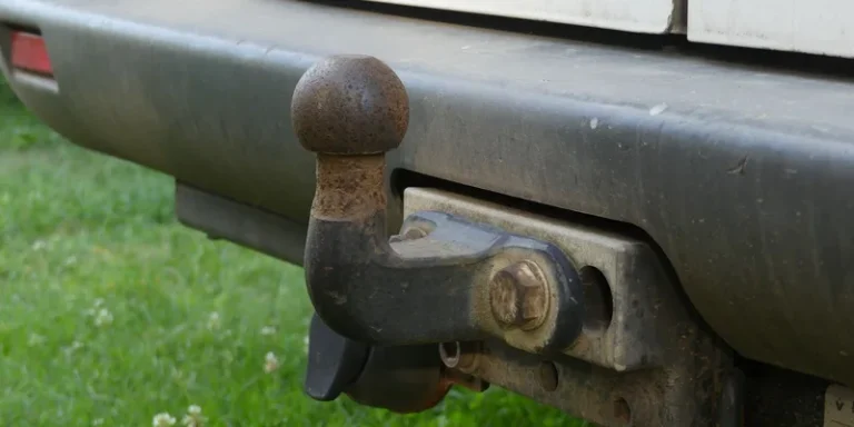 Close-up of a rusty tow hitch on the rear bumper of a vehicle against a grassy background
