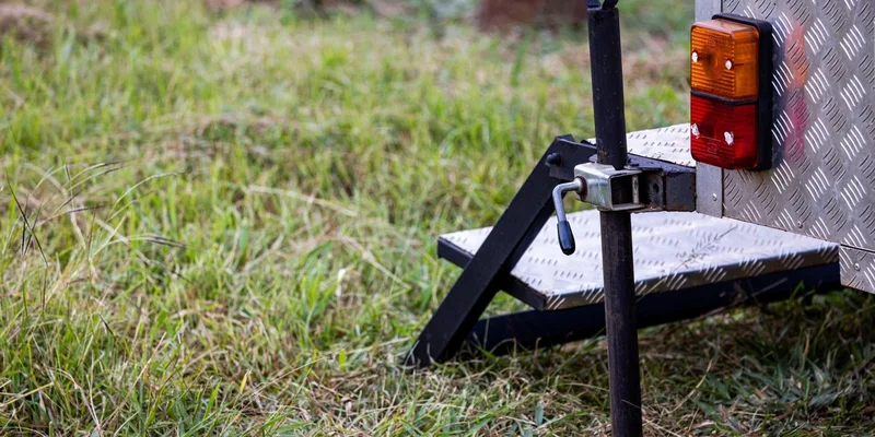 Close-up of a trailer hitch and jack on metal steps in a grassy field