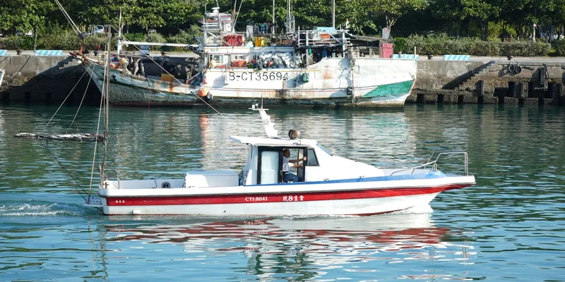 A motorboat cruises past moored fishing boats in a serene harbor setting