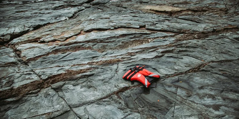 A red life vest rests on a rugged rocky shoreline by the sea, portraying solitude